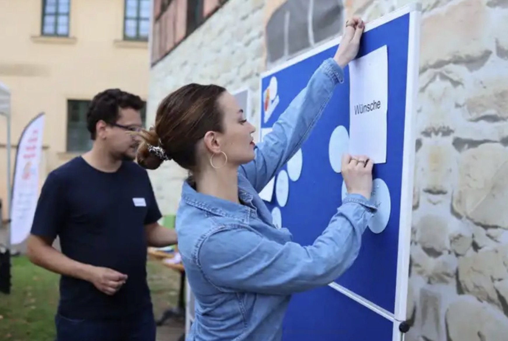Zwei Mitwirkende befestigen Karten an einer Stellwand